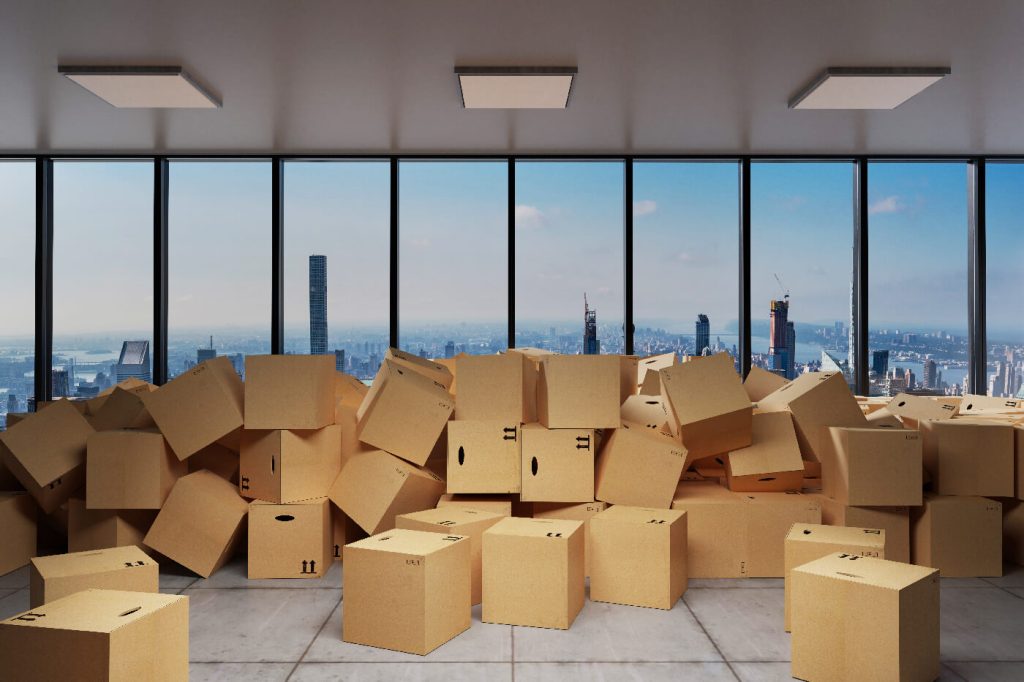 AdobeStock 368586776 1 large industrial urban warehouse with large pile of cardboard moving boxes in front of Skyline