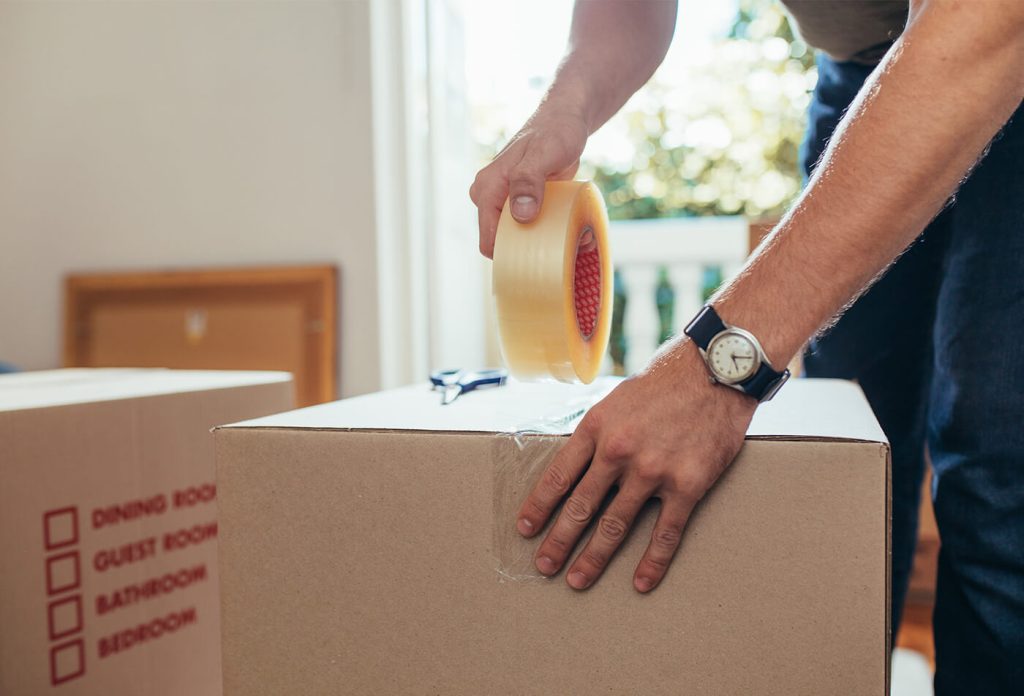 Close up of a man applying adhesive tape on a packing box Close up of a man applying adhesive tape on a packing box